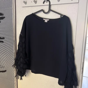 Mörkblå blus med fransiga ärmar H&M - Mörkblå blus från H&M med långa ärmar dekorerade med fransar och transparenta detaljer. Blusen har en rak passform och rund halsringning. Ärmarna har en unik struktur med inslag av mesh och fransar som ger en cool och trendig look.
