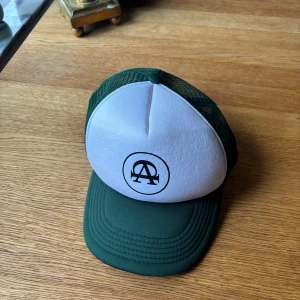Grön och vit keps från All Cap One - Snygg keps med grön skärm och mesh samt vit frontpanel med svart All Cap One -logga. Justerbar baktill för perfekt passform. Helt oanvänd!💚