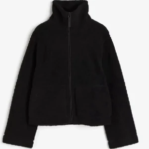 Svart teddyjacka med dragkedja - Mysig svart teddyjacka med hög krage och hel dragkedja framtill. Jackan har två stora fickor och är perfekt för kyliga dagar. Den har en enkel och stilren design som passar till många olika outfits.