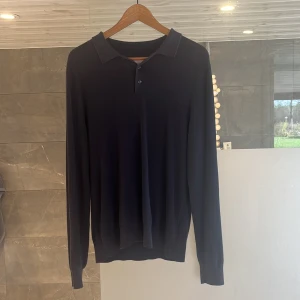 Svart pikétröja från These Glory Days - Klassisk svart långärmad pikétröja från These Glory Days i mjuk och skön bomull. Tröjan har krage, knäppning med två knappar och ribbade muddar vid ärmslut och nederkant. Perfekt för en clean och stilren look.