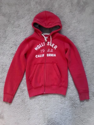 Röd zip up Hoodie Hollister  - Röd/korall färgad zip up Hoodie ifrån Hollister i storlek s, liten i storlek! Är lite urtvättad men är överlag i bra skick! 