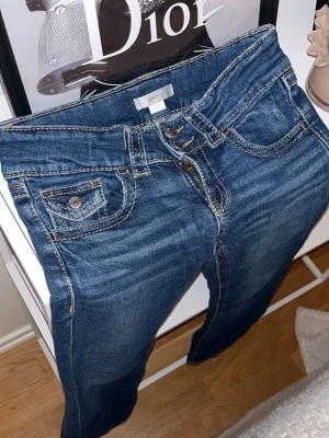 Blå bootcut jeans med kontrastsömmar - Säljer ett par klassiska blå jeans med bootcut-modell och snygga kontrastsömmar. Jeansen har fem fickor, bälteshällor och dragkedja med knapp. Jätte bra passform är tyvärr försmå för mig💕