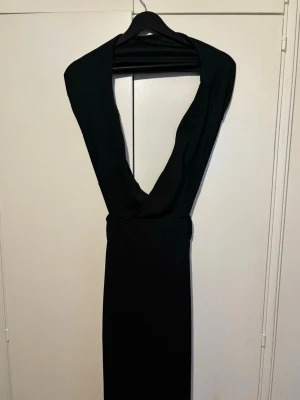 Festklänning  - Snygg svart långklänning med djup v-ringning och öppen rygg. Klänningen har en figurnära passform upptill och faller rakt ner med ett lätt utsvängt avslut. Materialet känns mjukt och har ett elegant fall. 