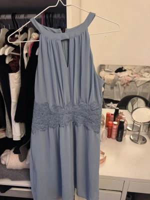 Ljusblå ärmlös klänning med spets - Säljer en ljusblå ärmlös klänning med vacker spetsdetalj i midjan och en liten v-ringning framtill. Klänningen har en mjuk, flowy passform och stängs med dragkedja i ryggen. Har endast blivit använd en gång.