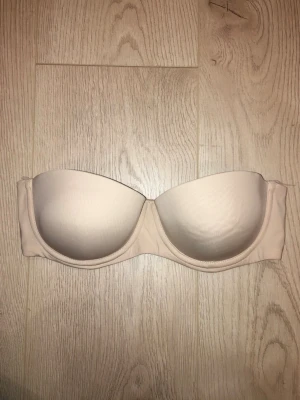 Beige axelbandslös bh  - Fin multifunktionell bh i fräscht skick. Storlek 75B i balconett modell. Axelbanden kan hakas av för en axelbandslös bh. Tyget är lent och slätt och i en beige färg. Väldigt bra bh för att ha under alla typer av plagg. Nyskick!