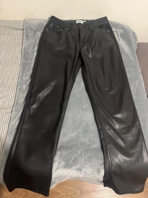 Svarta skinnbyxor  - Snygga svarta byxor från lager 157 i skinnimitation med klassisk femficksdesign och raka ben. Byxorna har normal passform och stängs med dragkedja och knapp framtill. Perfekt för dig som vill ha en cool och stilren look. Priset kan diskuteras