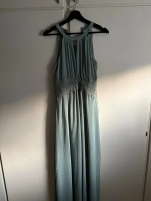 Ljusgrön  långklänning från Vila - Säljer en ljusgrön långklänning från Vila i storlek 36. Klänningen har spetsdetaljer i midjan, är ärmlös och har en v-ringad rygg. Materialet är mjukt och faller snyggt, perfekt för sommarens tillfällen. Snygg och stilren design.