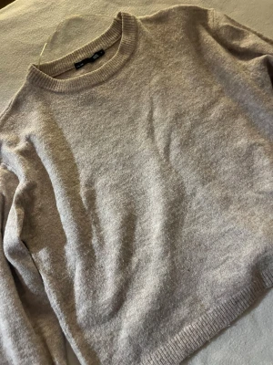 Beige stickad tröja  - Mysig beige stickad tröja från Pull&Bear i storlek XS. Tröjan har rund hals, ribbade muddar vid ärmslut och nederkant samt långärmad passform. Perfekt för lager-på-lager och chill dagar. Enkel och stilren design som funkar till det mesta.