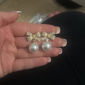 Ingen väst på bilden - Bilden visar ett par örhängen med rosett och pärla, ingen väst finns med.