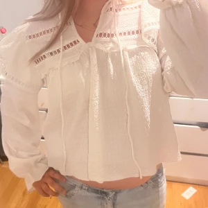 Vit blus med spets och band - Säljer en luftig vit blus med långa ärmar, v-ringning och dekorativa spetsdetaljer upptill. Blusen har knytband vid halsen och ett lätt strukturerat tyg som ger en cool vintagekänsla. Perfekt till jeans eller kjol för en fräsch look💕💕💕💕💕