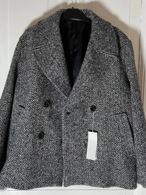Gråmelerad skepparkavaj i ull - Säljer en gråmelerad skepparkavaj från Arket i klassiskt fiskbensmönster. Jackan är dubbelknäppt med stora slag, har två framfickor och är tillverkad i ullblandning. Perfekt för höst och vinter när du vill vara både varm och stilren. Nypris 2790 kr. 