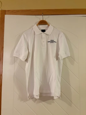 Vit Peak Performance pikétröja - Ny och oanvänd vit pikétröja från Peak Performance med klassisk krage och två knappar framtill. Tröjan har korta ärmar och diskret logga på bröstet. Materialet är mjuk bomull som känns skönt mot huden. Perfekt för dig som gillar stilren och sportig look.