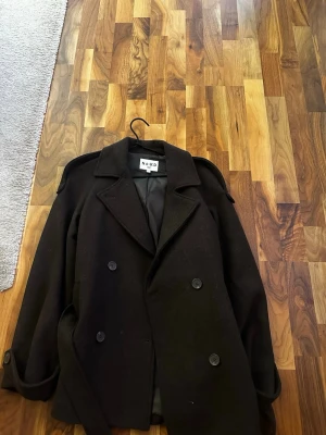 Svart tjock kavaj från NA-KD - Säljer en svart skepparkavaj från NA-KD med klassisk dubbelknäppning och breda slag. Jackan har axelklaffar och knappar vid ärmsluten för extra stilpoäng. 