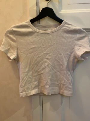 Vit ribbad croppad topp från Even&Odd - Säljer en vit croppad topp från Even&Odd med ribbad struktur. Toppen har rund halsringning och korta ärmar, perfekt att matcha med jeans eller kjol. Materialet är mjukt och stretchigt, vilket gör den bekväm att bära hela dagen.