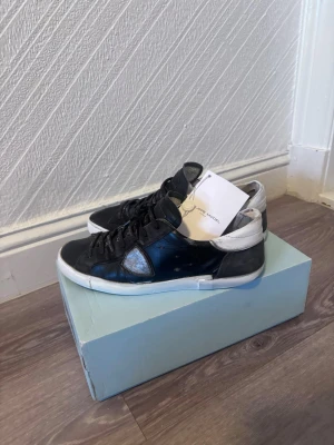 Svarta Philippe Model sneakers - Säljer ett par svarta Philippe Model sneakers med vit sula och grå detaljer vid hälen. Skorna har snörning med svarta skosnören där märket står tryckt. Ovandelen är i skinn och har en rund tå. Snygg och stilren design som passar till många outfits.