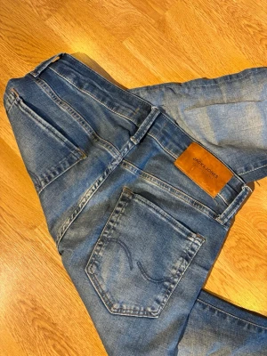 Jack & Jones Slim Glenn jeans blå - Slim Glenn jeans från Jack & Jones i klassisk blå tvätt med snygga slitningar. Modellen har fem fickor, knappgylf och brunt läderpatch bak i midjan. Jeansen är smala i benen och har en modern passform som sitter snyggt. Perfekt för dig som gillar stilrena och bekväma jeans. Vid frågor är det bara att skriva! Kom med bud!