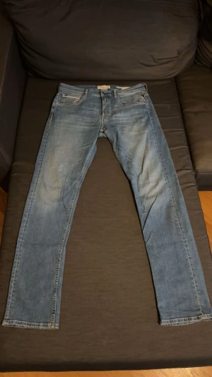 Replay ljusblå jeans, storlek 31/32 - Säljer ett par snygga ljusblå jeans från Replay med klassisk femficksdesign och läderpatch bak. Jeansen har raka ben och diskreta slitningar framtill för en cool look. Passar dig som gillar stilrena och tidlösa jeans.