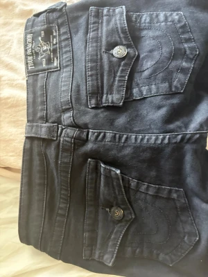 Svarta True Religion  - Svarta true religion jeans i modellen joey. De är lågmidjade och bootcut. Finns lite slitningar längst ner men annars inga skador. Byxorna är använda få gånger. Jag säljer eftersom de är för stora. ☺️ priset kan diskuteras 👍🏼