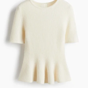 Vit stickad topp från H&M - Supersöt vit stickad topp från H&M med korta ärmar och rund hals. Tröjan har en ribbad struktur och en peplum-liknande volang nedtill som ger en snygg siluett. Perfekt för dig som gillar en clean och chic stil.