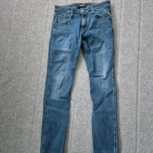 Replay blå jeans slim fit W29 L32 - Snygga blå jeans från Replay med klassisk femficksdesign och diskret Replay-logga på fickan. Modellen har slim fit och raka ben, med kontrastsömmar och normal midja. Perfekt för dig som gillar stilrena och bekväma jeans.