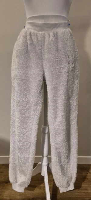 Fluffiga vita mjukisbyxor i storlek M från Cubus - Supermysiga vita mjukisbyxor med fluffig yta och bred ribbad midja. Perfekta för chill hemma eller när du vill vara extra bekväm. Byxorna har muddar vid bensluten och en relaxed passform som ger skön rörelsefrihet. Midjebredd ca 40 cm och innerbenslängd ca 74 cm med mudden. Material 100 % polyester. Brodyr på en Höft.