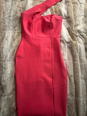 Rosa one shoulder klänning med slits - Snygg rosa klänning med one shoulder-design och figurnära passform. Klänningen är lång och har en slits framtill för extra edge. Materialet är slätt och stretchigt, perfekt för dig som vill sticka ut. Passar dig som gillar trendiga och stilrena plagg.