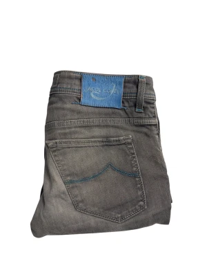 Grå jeans från Jacob Cohen, stl 33 - Snygga grå jeans från Jacob Cohen med raka ben och klassisk femficksdesign. De har blå kontrastsömmar och ett blått märke bak i midjan. Jeansen är tillverkade i bomull och har en normal passform. Perfekt för dig som gillar stilrena och exklusiva detaljer.