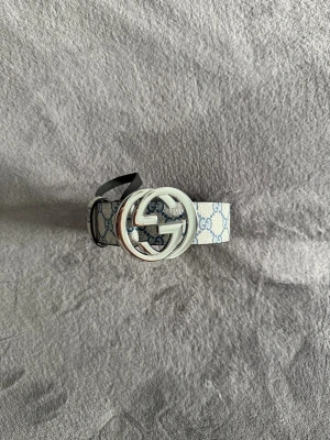 Gucci bälte  - Gucci GG Supreme bälte med klassiskt monogrammönster i blått på beige bakgrund. Bältet har en stor rund silverspänne med dubbla G-loggan och insida i ljust brunt skinn. Perfekt för att lyfta vilken outfit som helst.