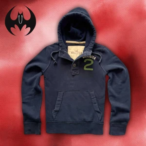 Mörkblå Hollister hoodie med tryck - Mörkblå hoodie med tryck och grön markering på bröstet från Hollister | Size M | Längd: 65cm Axelbredd: 44cm Armlängd: 70cm | Passar mellan 170-185cm