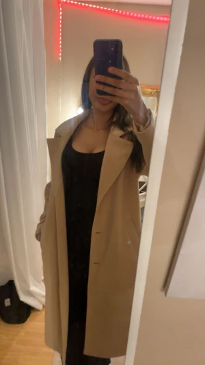 Beige lång kappa med klassisk krage - Säljer en beige kappa med snygg klassisk krage och rak passform. Jackan har långa ärmar och dolda knappar framtill. Perfekt för dig som gillar stilrena och tidlösa plagg. Fickor på sidorna för extra funktionalitet.💞(är 172 lång)