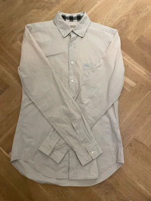 Beige skjorta från Burberry Brit - Stilren beige skjorta från Burberry Brit med klassisk krage, långa ärmar och knäppning framtill. Skjortan har diskret broderad logga på bröstet och rutigt mönster på insidan av kragen. Tillverkad i mjuk bomull för en clean och bekväm look. I storlek S✌️
