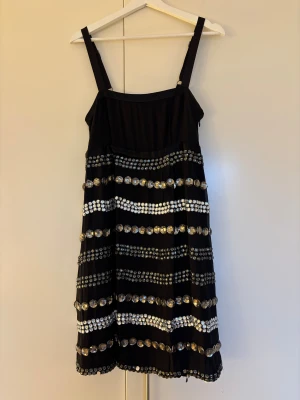 By Malene Birger svart sidenklänning med stenar - By Malene Birger svart sidenklänning med stenar. Reglerbara axelband och justerbara spännen. Fodrad. Klänningen har flera rader av stora och små glittriga stenar i silver som gör den till den perfekta nyårsklänningen! Storlek 38, passar även 36.