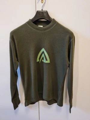 Mörkgrön långärmad tröja från Aclima strl 150 (barn) - Säljer en mörkgrön långärmad tröja från Aclima med deras logga tryckt på bröstet i storlek 150, barnstorlek. Tröjan är tillverkad i mjuk och varm 100% merinoull, perfekt för kyliga dagar. Små hål förekommer, se bilder.