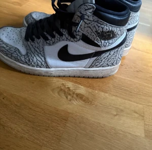 Nike Jordan 1 Elephant Print Highs - Säljer ett par Nike Jordan 1 Highs med grymt elefantmönster i grått och svart. Skorna har svart swoosh, snörning och vit bas i skinn. Perfekt för dig som vill sticka ut med klassiska sneakers med unik design.