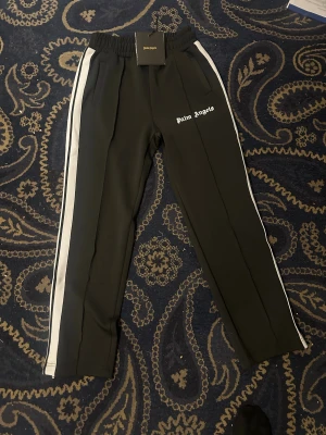 Svarta Palm angels byxor Storelk S - Palm Angels-byxor, storlek S. Helt nya, aldrig använda. Stilren design med hög kvalitet – perfekta för en trendig och sportig look.