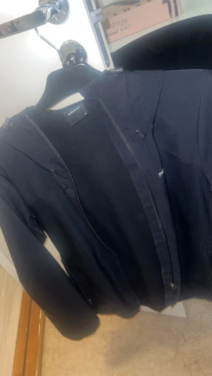 Svart Peak Performance jacka, strl M - Svart jacka från Peak Performance i storlek M. Har huva, full dragkedja och diskret logga på bröstet. Materialet är slätt och vindtåligt – perfekt för blåsigare dagar. Snygg och enkel design med långa ärmar och praktiska fickor. I mycket bra skick, sparsamt använd.