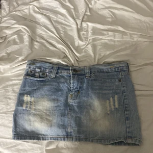 Ljusblå jeanskjol från ZPJ - Säljer en gammal ljusblå jeanskjol från ZPJ med slitna detaljer framtill och broderad ficka bak. Kjolen har klassiska fickor, bälteshällor och knappstängning. Med en fin detalj på ena bakfickan Perfekt för dig som gillar en avslappnad och trendig stil.