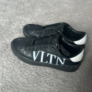 Valentino opens svartvita - Snygga svarta sneakers från Valentino med vit VLTN-logga på sidan. Skorna har en klassisk design med snörning och en vit detalj på hälen. Perfekta för en stilren look. Vid frågor är det bara att skriva. Buda ifall ni är intresserade