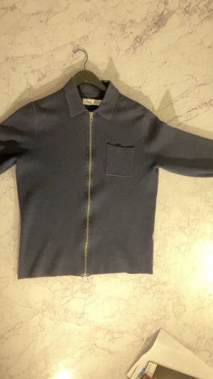 Mörkblå overshirt med dragkedja - Snygg mörkblå overshirt från Schnayderman's med klassisk krage, bröstficka och guldfärgad dragkedja framtill. Jackan har lång ärm och en stilren, rak passform som funkar till många olika looks. Perfekt för dig som gillar minimalistisk design.