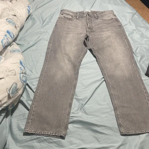 Grå jeans från Jack & Jones - Snygga grå jeans från Jack & Jones med en klassisk straight passform. De har en normal midja och är perfekta för en avslappnad stil. Jeansen har fem fickor och stängs med dragkedja och knapp.