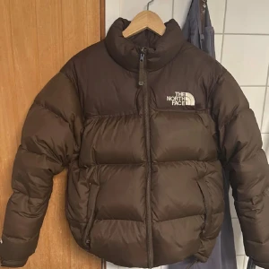 Brun pufferjacka från The North Face - Fin jacka från the north face väldigt sparsamt använd och i fint skick. Storlek S, perfekt för vinter/höst. Nypris är runt 4 tusen kronor. Fler bilder kan skickas, pris kan diskuteras vid snabb affär. 