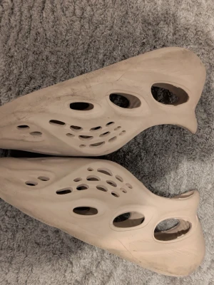 Beige slip-on sandaler med hålmönster - Unika beige sandaler med futuristisk design och många hål för extra ventilation. Tillverkade i lätt syntetmaterial, perfekta för chill dagar eller som statement piece. Skorna har rund tå och platt sula för skön komfort.