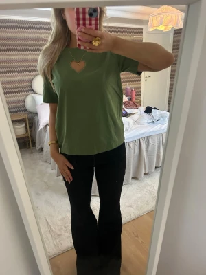 Cloeys topp - Cloeys topp! Snygg grön t-shirt i bomull med korta ärmar och en unik hjärtformad cut-out vid halsen. Passformen är normal och tyget känns mjukt och skönt. Perfekt för dig som vill ha något enkelt men ändå med en twist.