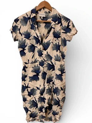 Blommig byxdress från Ganni XS - Säljer en beige byxdress från Ganni i storlek XS med blått och grått blommönster. Byxdressen har korta ärmar, krage och resår i midjan för en skön passform. Perfekt för dig som vill ha en chill och snygg sommarlook.