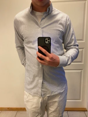 Randig skjorta Clean Cut Copenhagen M - Säljer en snygg randig skjorta från Clean Cut Copenhagen i storlek M. Skjortan har smala gråa och vita ränder, klassisk krage och knäppning framtill. Tillverkad i bomull, polyester och lite stretch för extra komfort. Perfekt till jeans eller chinos.