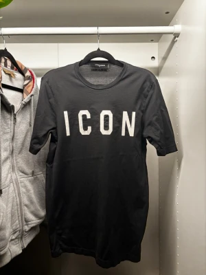 Svart ICON t-shirt från Dsquared2 - Snygg svart t-shirt från Dsquared2 med stor vit 'ICON'-text på bröstet. Klassisk rund hals och korta ärmar. Tillverkad i mjuk bomull som känns skön mot huden. Perfekt för dig som vill ha en clean och trendig look.