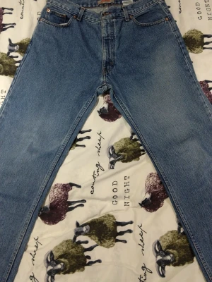 Blå raka jeans från Plaza - Säljer ett par klassiska blå jeans från Plaza i modellen Key West. Jeansen har raka ben, fem fickor och snygga kontrastsömmar. Tillverkade i 100% bomull för en autentisk jeanskänsla. Perfekta till sneakers eller boots och funkar året runt.