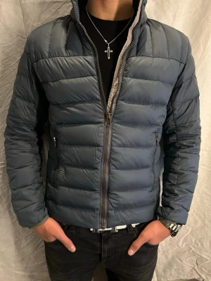 Mörkblå pufferjacka från Colmar - Säljer en mörkblå pufferjacka från Colmar med hög krage och två dragkedjeförsedda fickor. Jackan har quiltad design och Colmar-logga på ärmen. Perfekt för kyliga dagar och riktigt snygg till jeans.