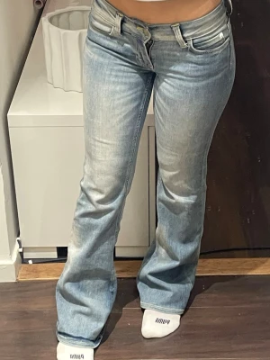 Ljusblå bootcut jeans från Cheap Monday - Säljer ett par ljusblå jeans från Cheap Monday med bootcut-passform och låg midja. Jeansen har klassisk femficksdesign, snyggt slitna detaljer och en stor vit logopatch bak i midjan. Perfekta för dig som gillar en avslappnad och trendig look.