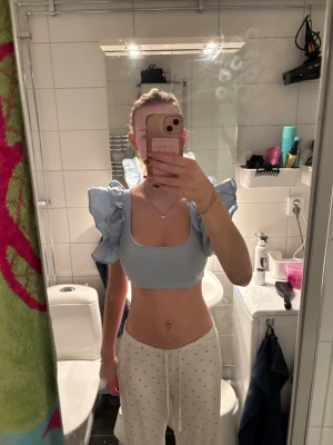 Ljusblå croppad topp med volangärmar - Säljer en ljusblå croppad topp med stora volangärmar och fyrkantig urringning. Toppen är ärmlös med breda axelband och har en trendig, feminin look. Perfekt för dig som vill sticka ut med en söt och modern stil.